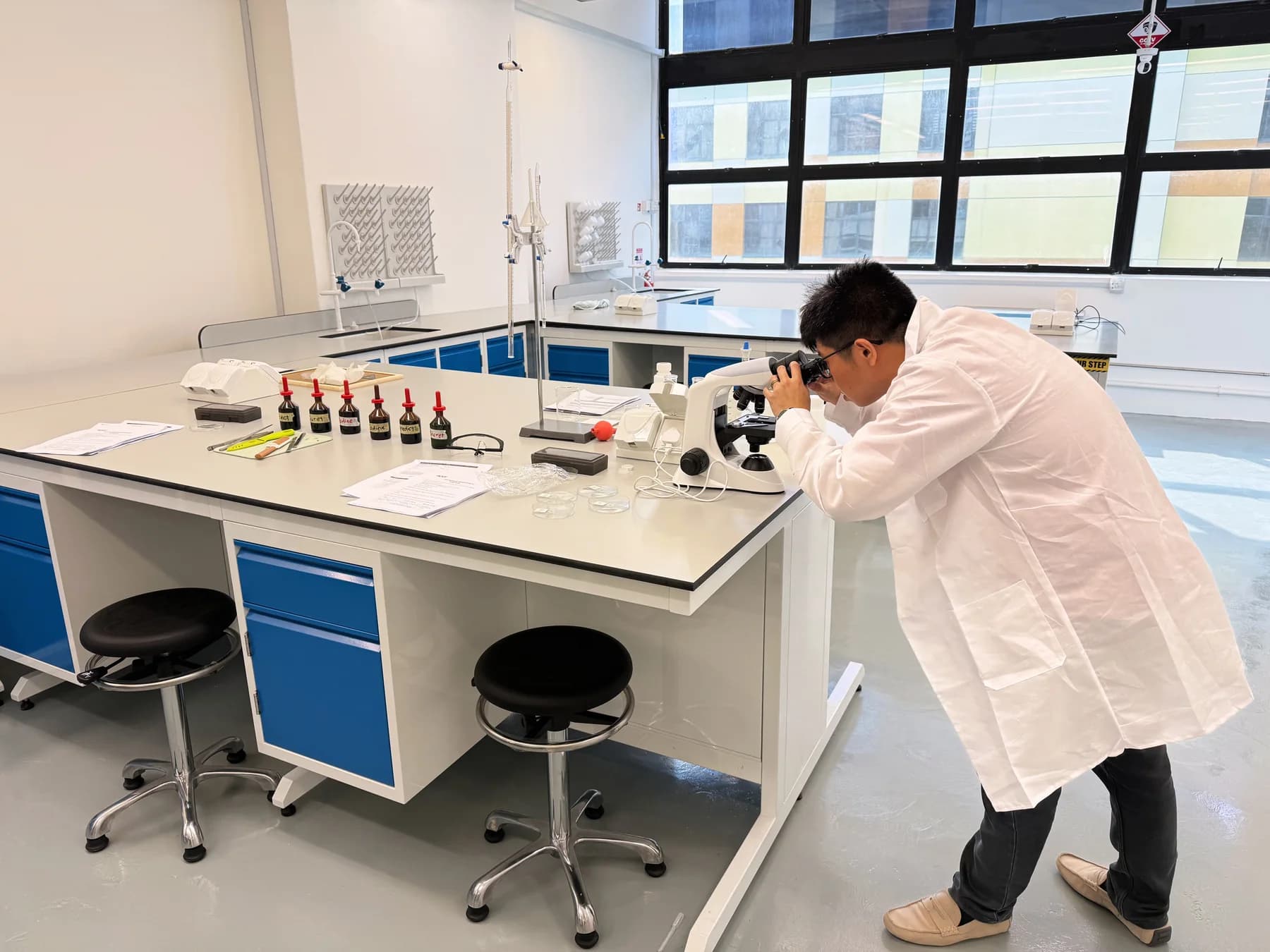 A student using a microscope at a blue-and-white laboratory bench at Eclat
